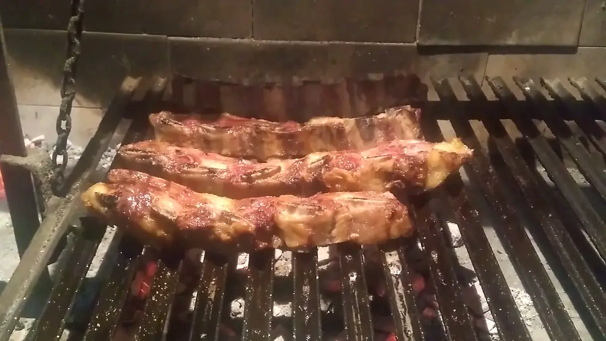 Chorizos y carne sobre la parrilla, con las brasas debajo.
