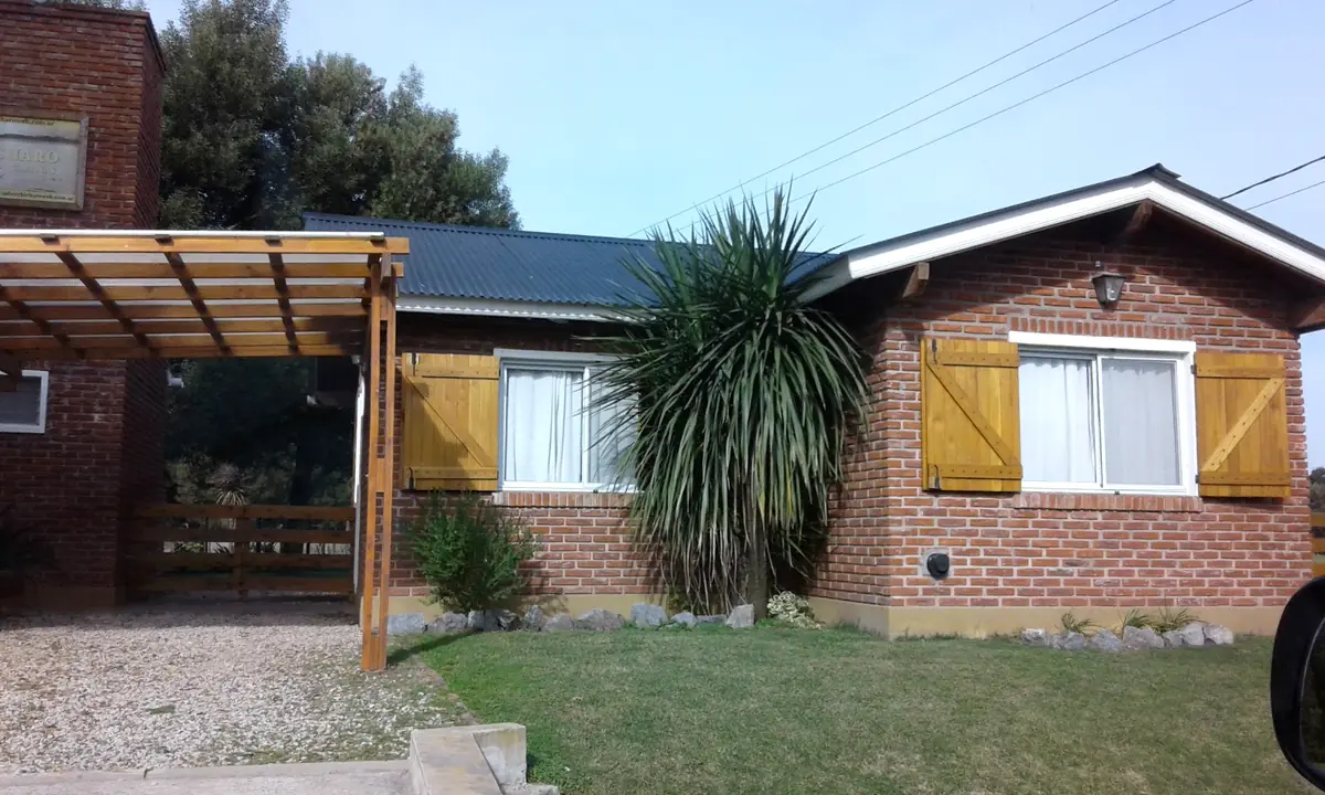 Una de las cabañas: ladrillo a la vista, postigos de madera, una palmera y la galería techada a un costado.