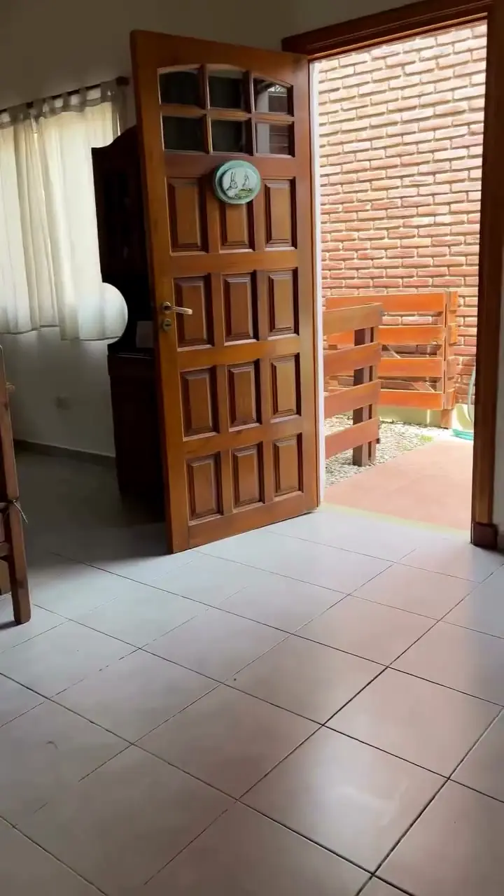 La puerta de madera de la cabaña, abierta hacia la galería de ladrillo.