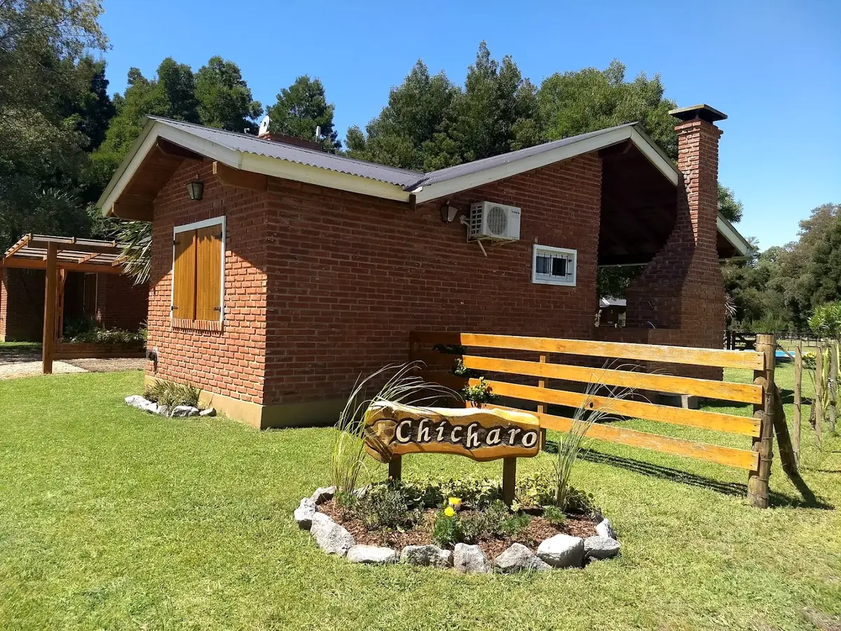 El cartel de madera de Chícharo sobre el césped, rodeado de piedras, delante de una cabaña.
