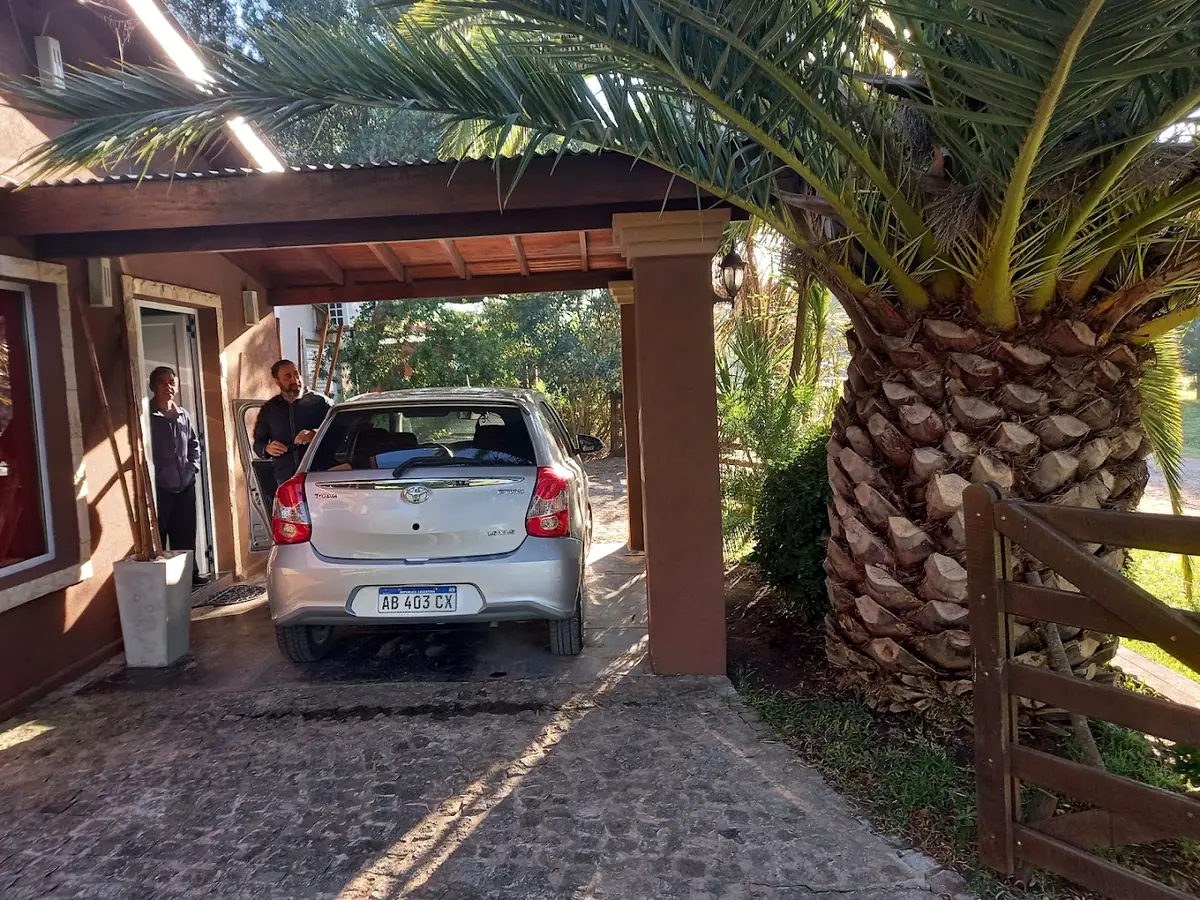 La cochera cubierta con pérgola de madera junto a una palmera, en la entrada de una de las cabañas.